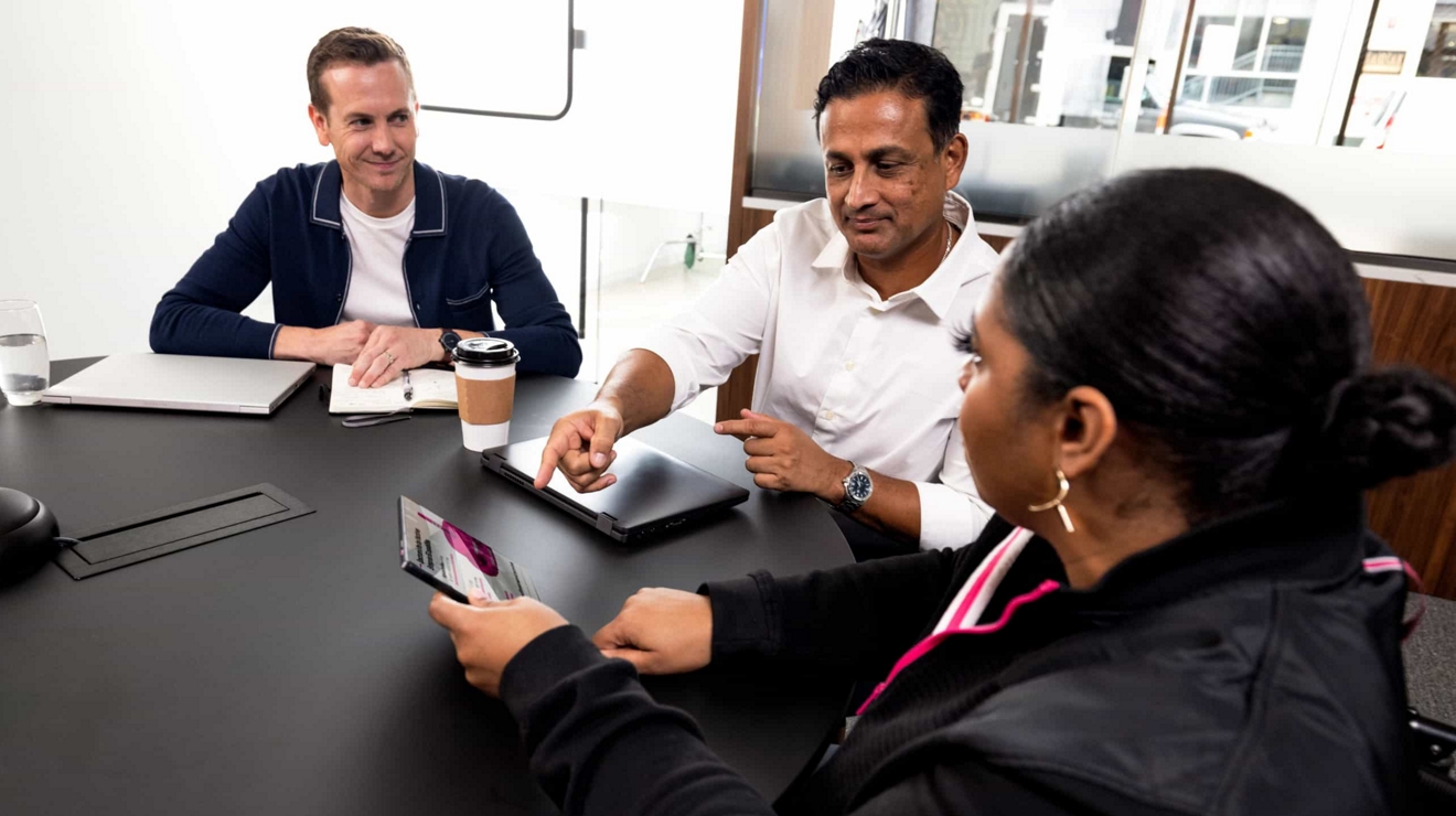 A group of government employees in a meeting room discuss information they see on a tablet.