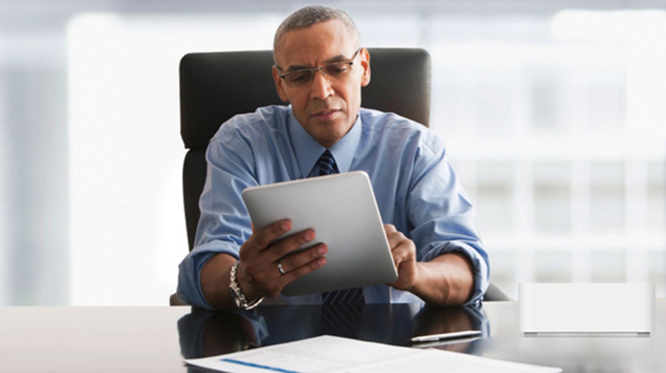 Man at office desk with glasses looks at tablet