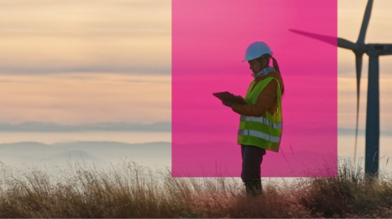 A wind energy engineer checks her tablet on a wind farm at dawn.