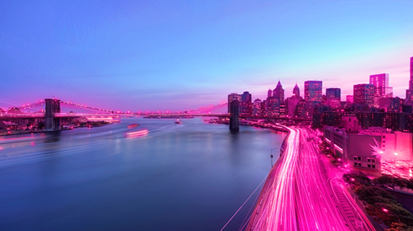 Highway and cityscape along a waterway, with magenta light along horizon