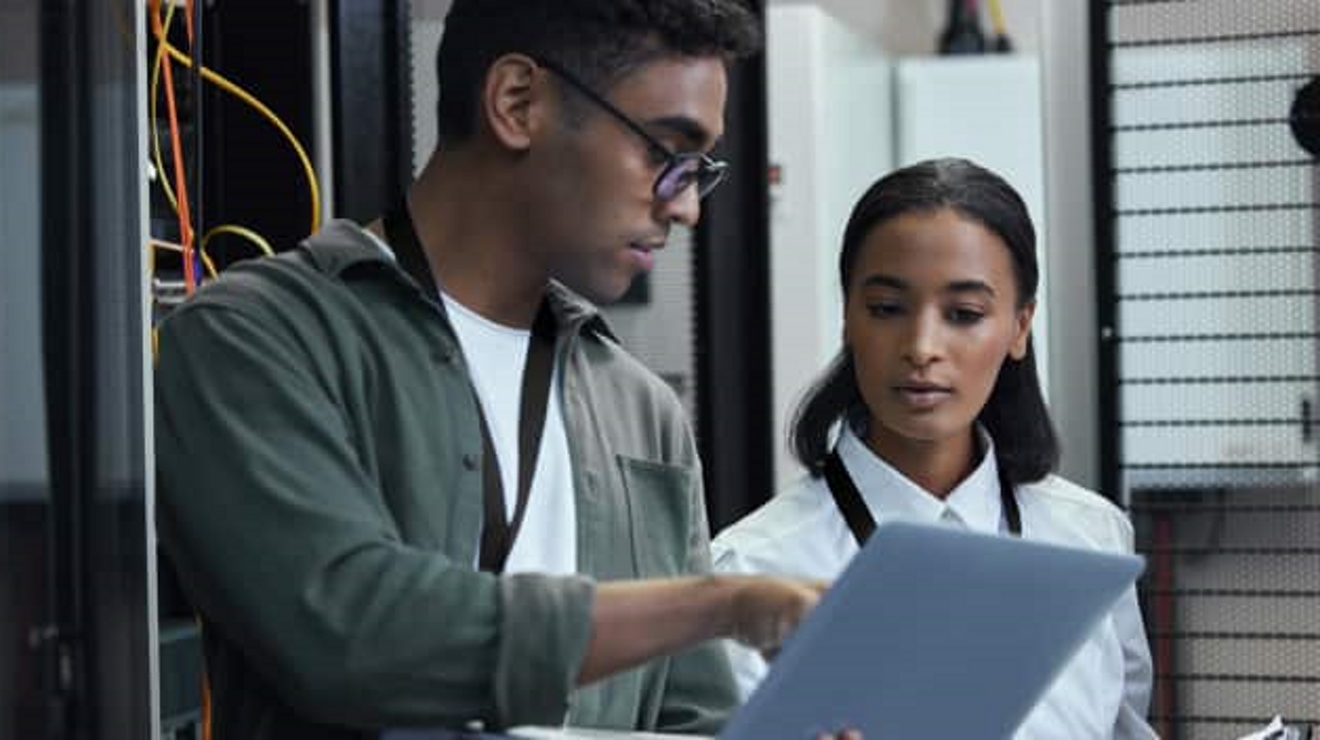A professional holds a laptop and points at the screen to show it to his coworker.