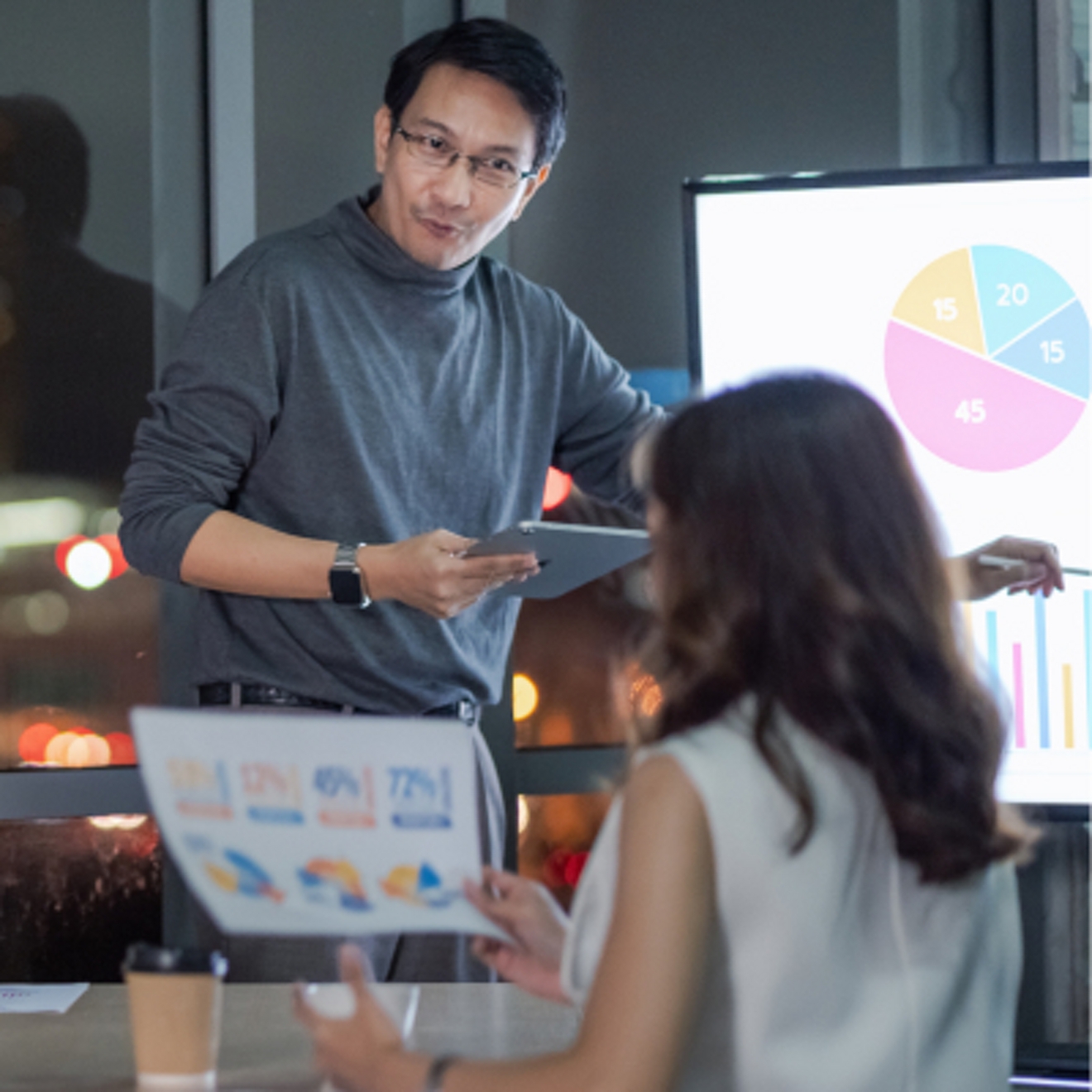 A businessperson displays several charts on a video screen and presents them to a coworker.