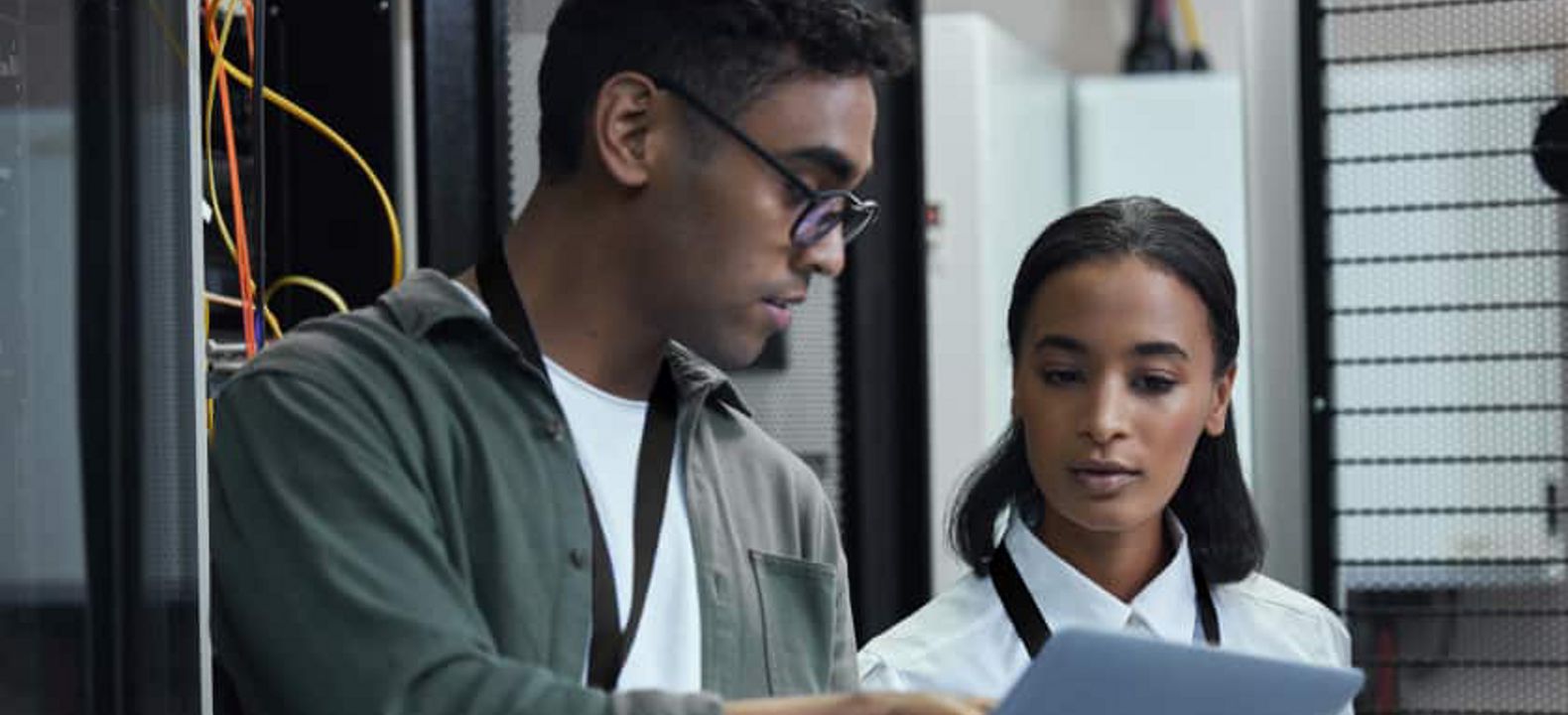 A professional holds a laptop and points at the screen to show it to his coworker.