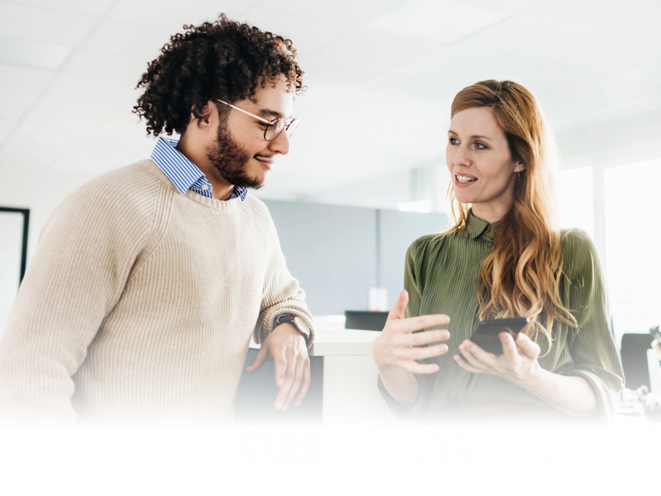 Two professionals in an office review information on one of their smartphones.