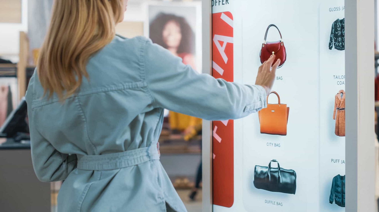 A clothing store shopper selects an image of a handbag from an interactive kiosk.
