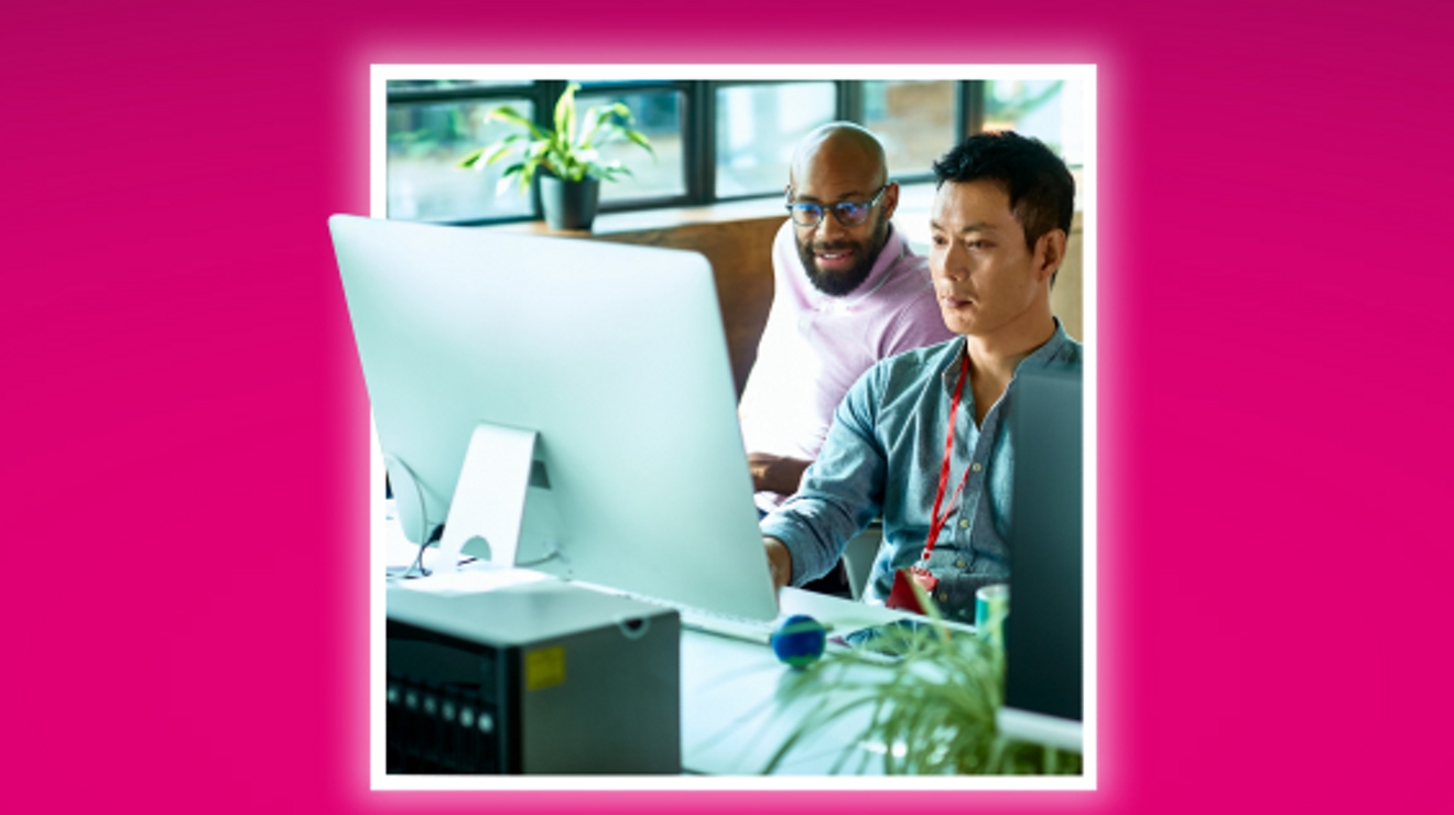 Two seated colleagues collaborate over a desktop computer.