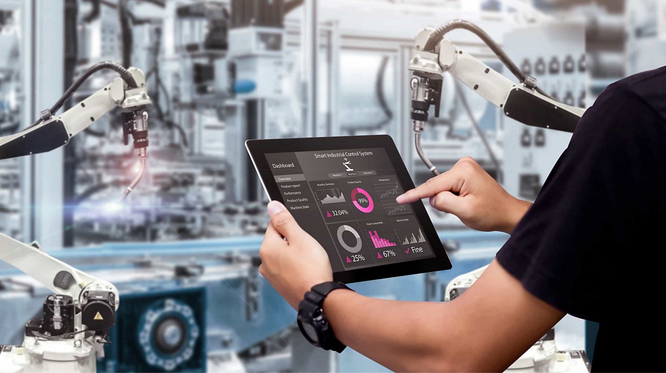 A person monitors automated industrial machinery with a touchscreen dashboard on a connected tablet.