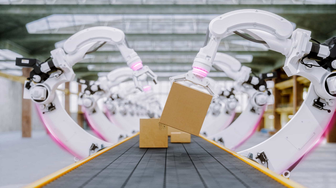 Robotic arms pick up cardboard packages that are moving on a long conveyor belt.