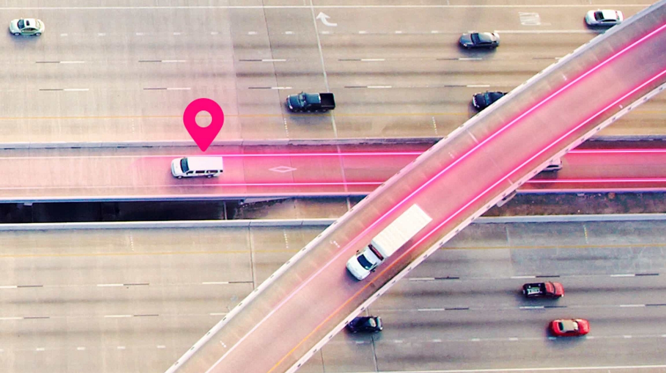 Aerial view of a highway. A magenta location pin and paths indicate fleet tracking for two vehicles.