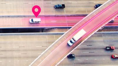 Overhead view of two trucks, one below a geolocation icon, traveling on a magenta-glowing highway.