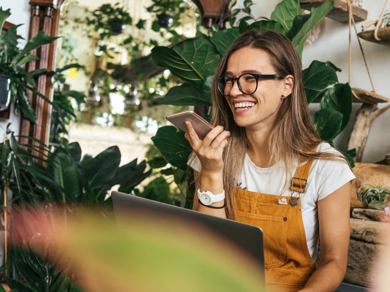 An employee at a plant shop smiles as they talk on their smartphone.