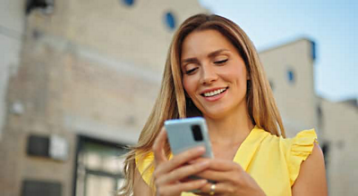 A smiling woman looks down at her smartphone.