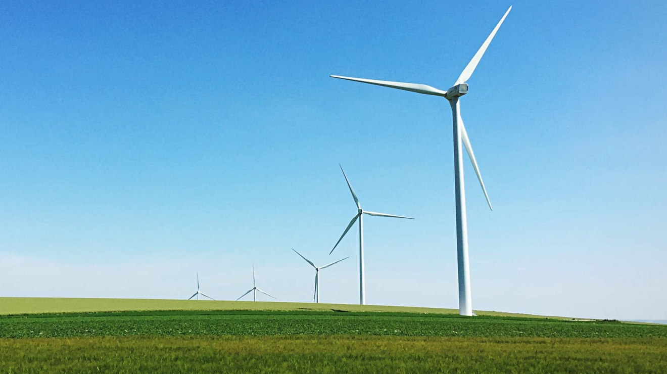 A row of windmills in a line across a large agricultural field.