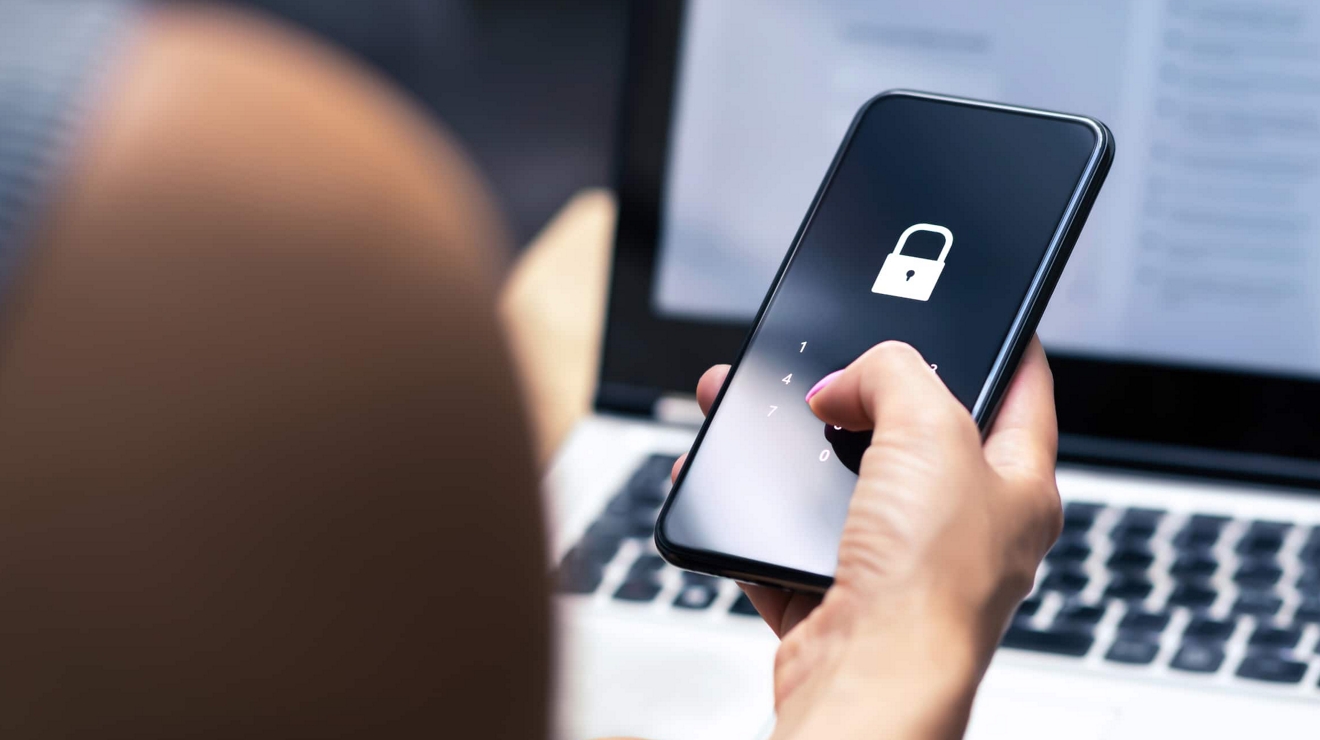Over-the-shoulder view of a lock screen on a smartphone and a laptop in the background.