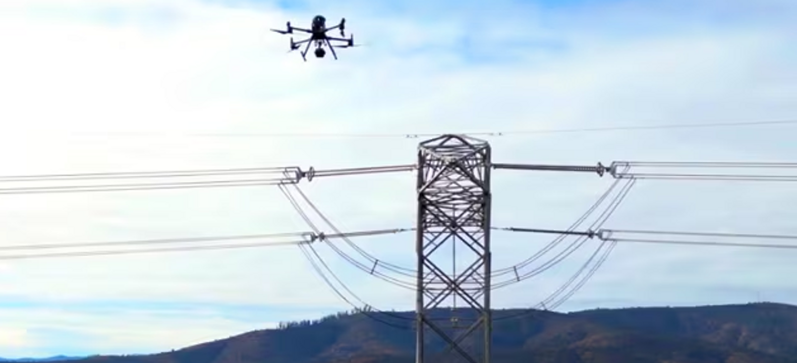 A connected drone hovers over a power-line pylon, using computer vision to help inspect the energy infrastructure.