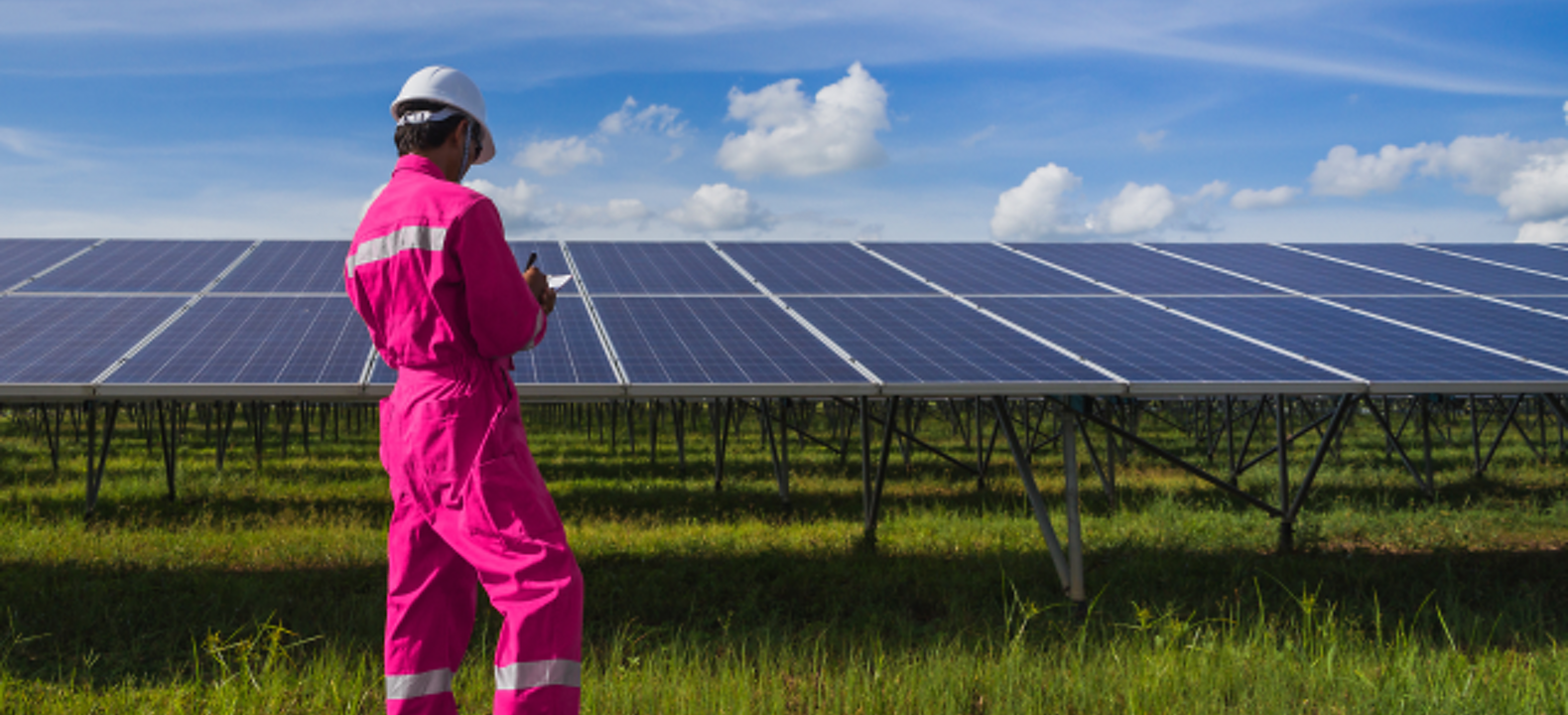 An energy technician in magenta coveralls examines panels at a solar power facility.