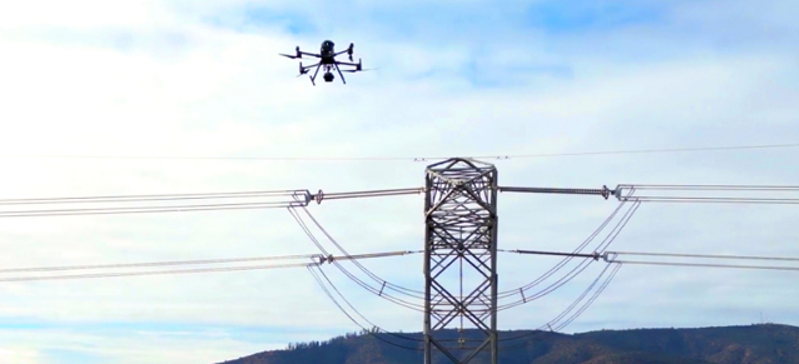 A connected drone hovers over a power-line pylon, using computer vision to help inspect the energy infrastructure.