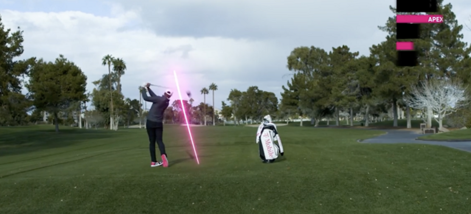 A golfer completes his swing next to his T-Mobile golf bag; while the the path of the ball is tracked in magenta.