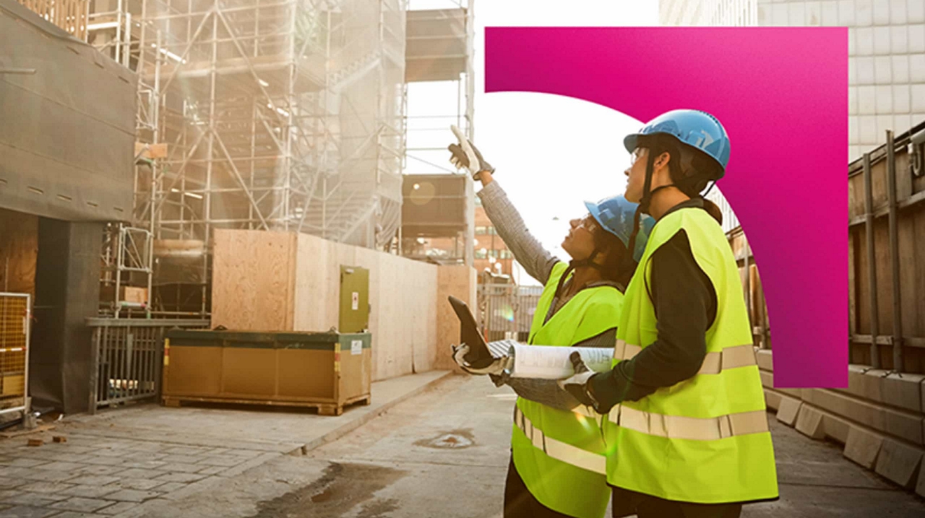 Two workers outside a construction site reference a digital tablet and discuss the project. 