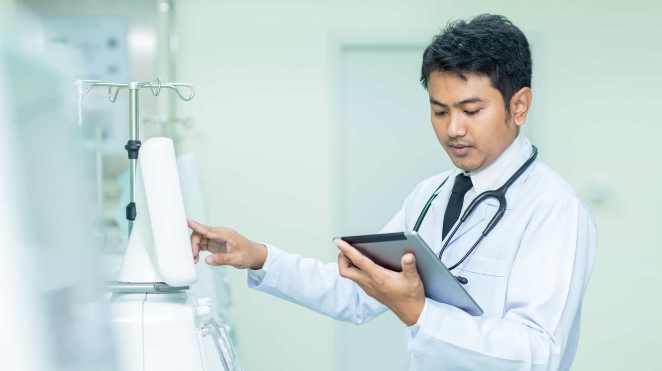 A doctor touches a medical device and reviews information on a tablet.