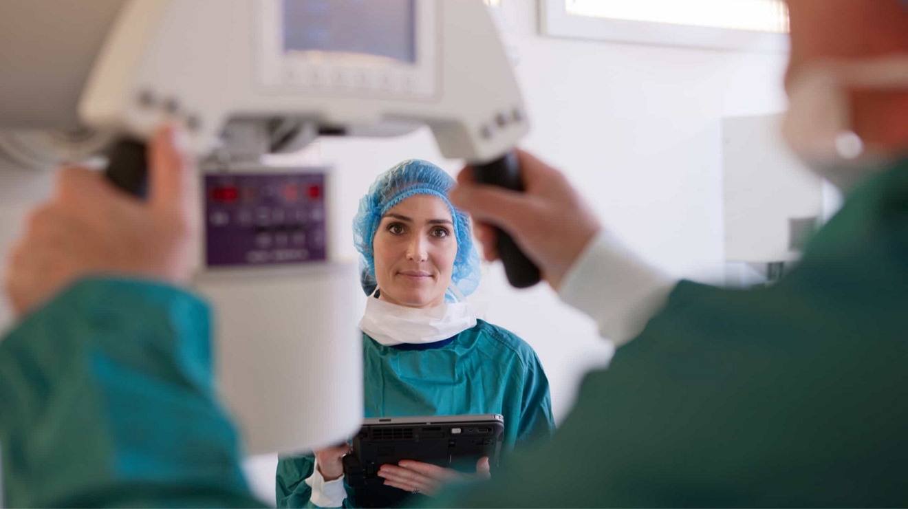 A healthcare professional operates a medical device while another observes with a device in-hand. 