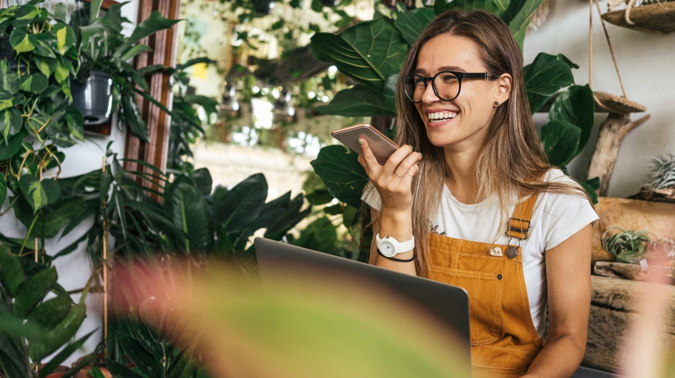 A worker at a plant shop sits and smiles while talking on her cell phone.