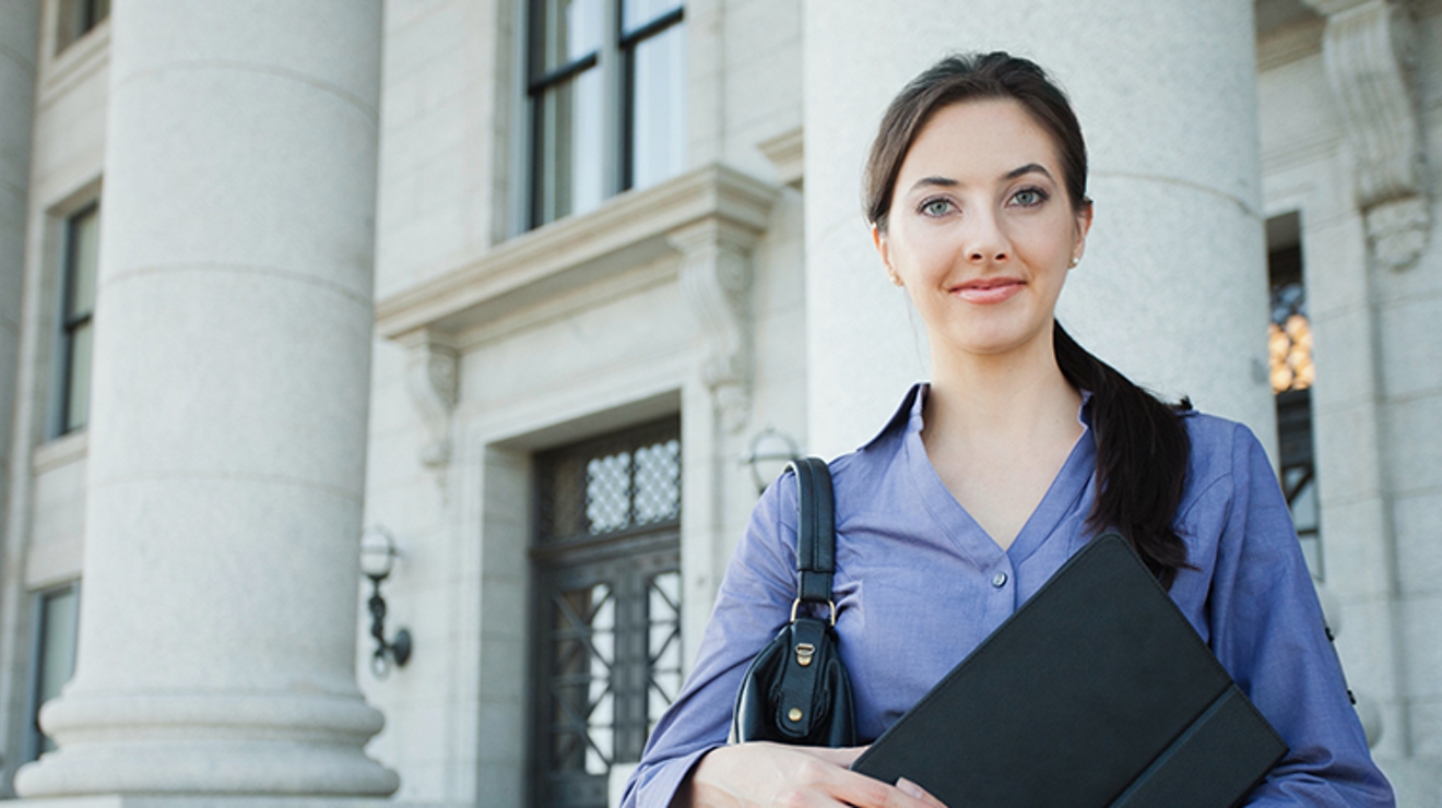 A government employee stands outside a government building holding a connected tablet.