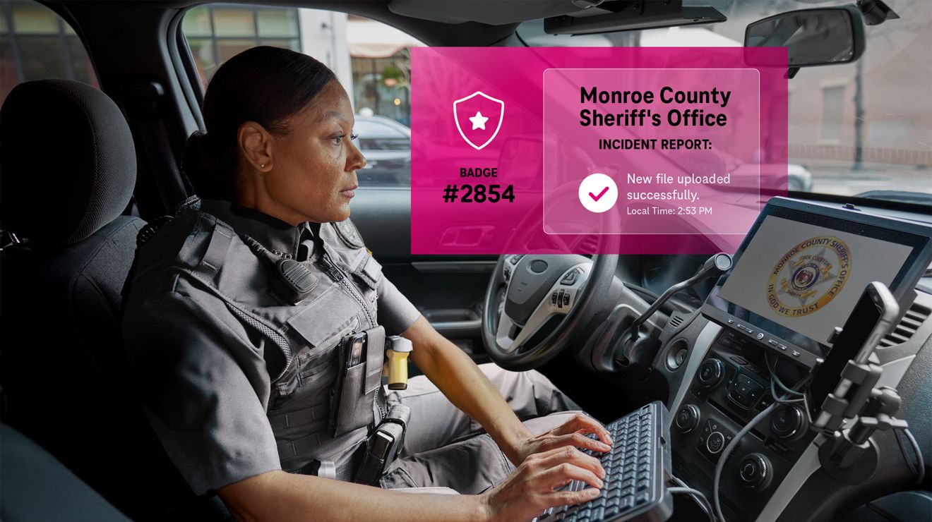 A police officer files a report, in a patrol car, using a dashboard screen and a connected keyboard.