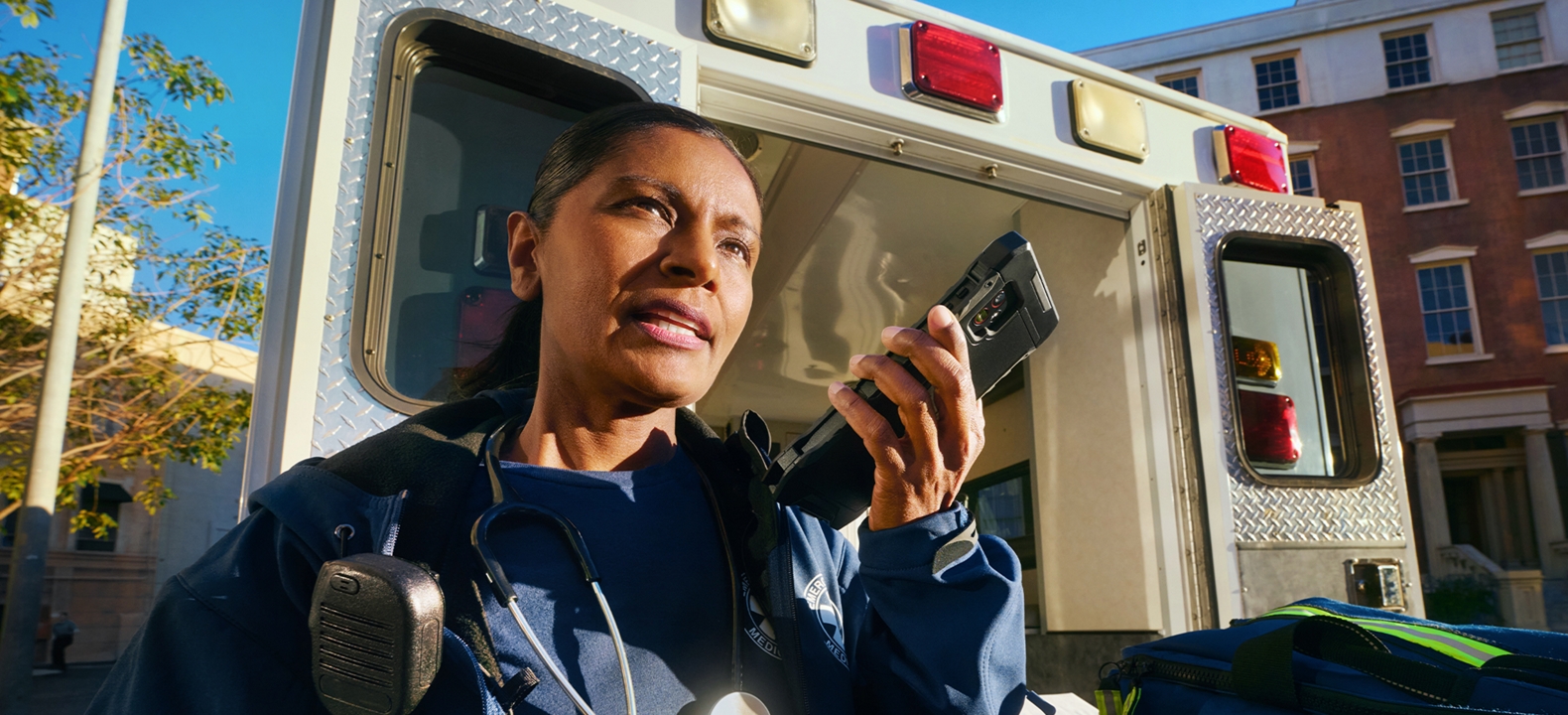 A first responder uses a walkie-talking while standing by an emergency vehicle. 