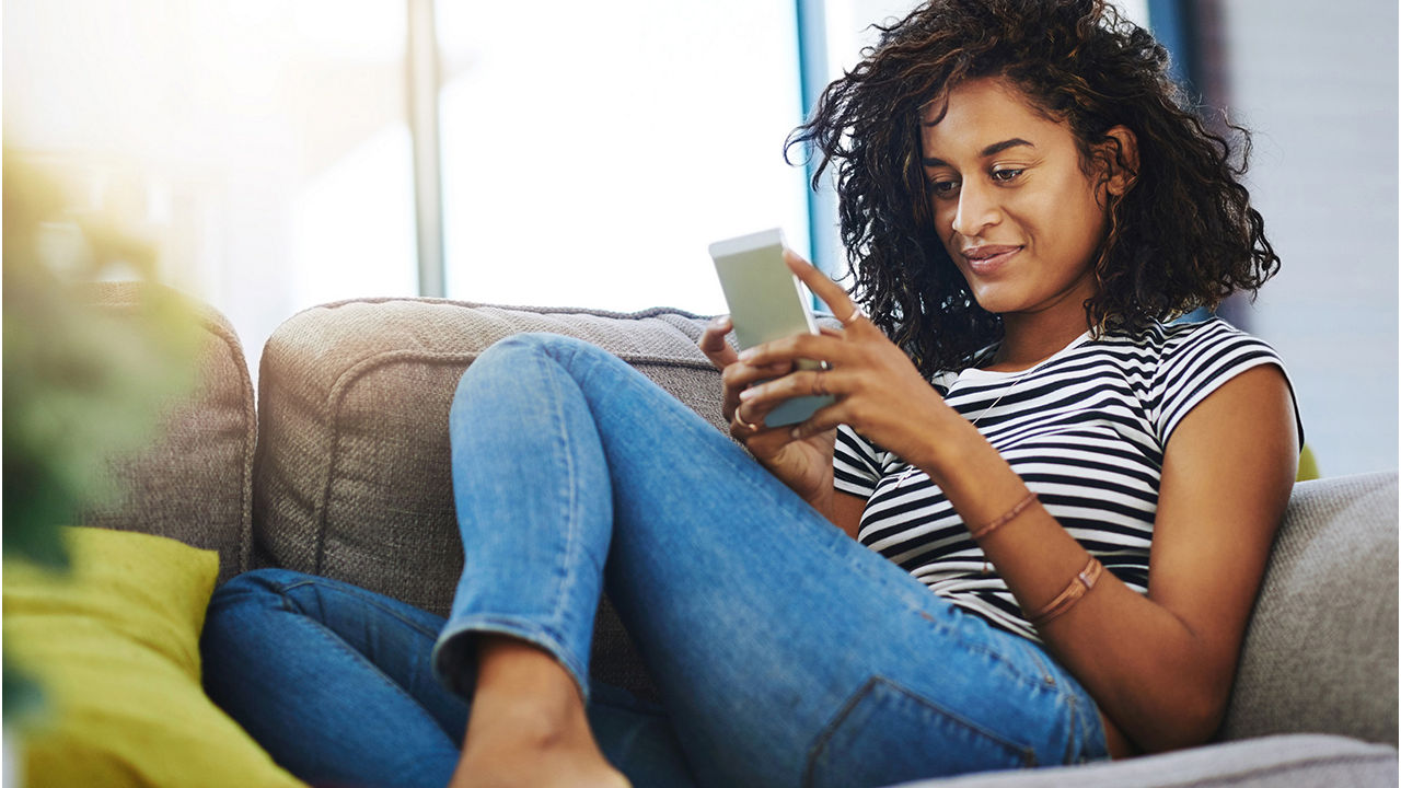 Woman looking at her phone while sitting comfortably on a couch.