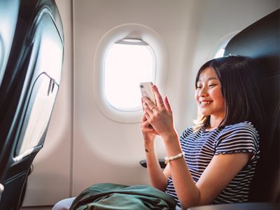 Airline passenger happily using her phone midflight.