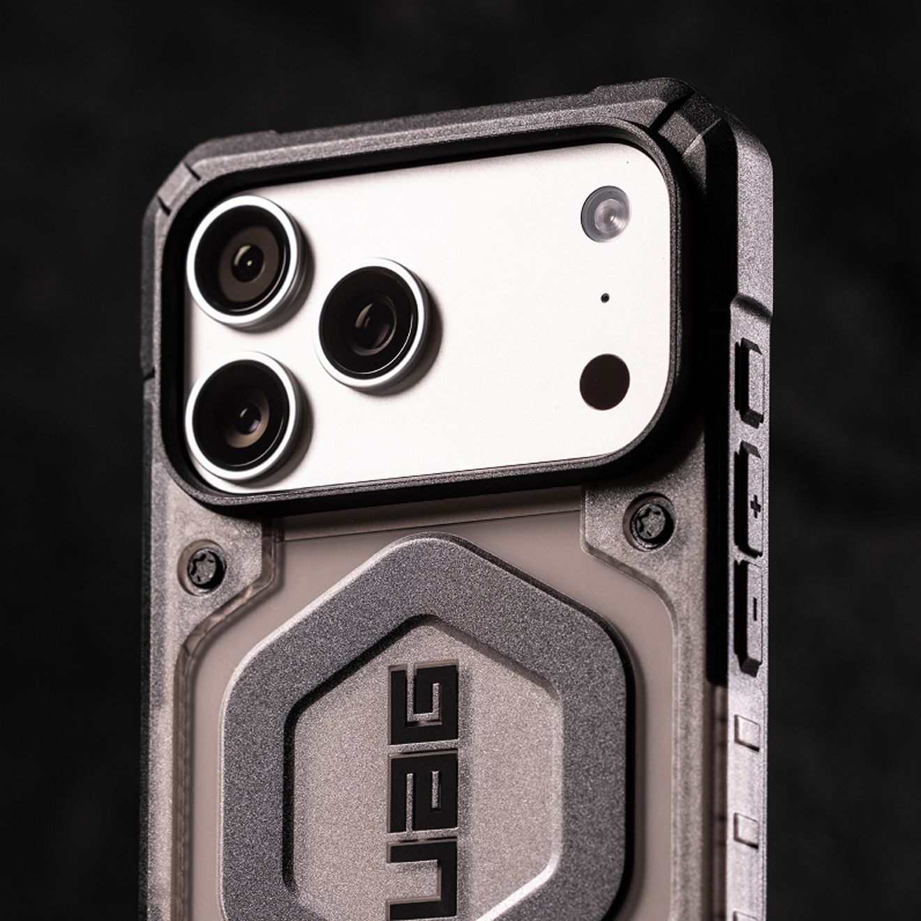 Close-up of a silver iPhone Pro Max's triple-lens camera system protected by a rugged gray UAG case with reinforced edges and side buttons.