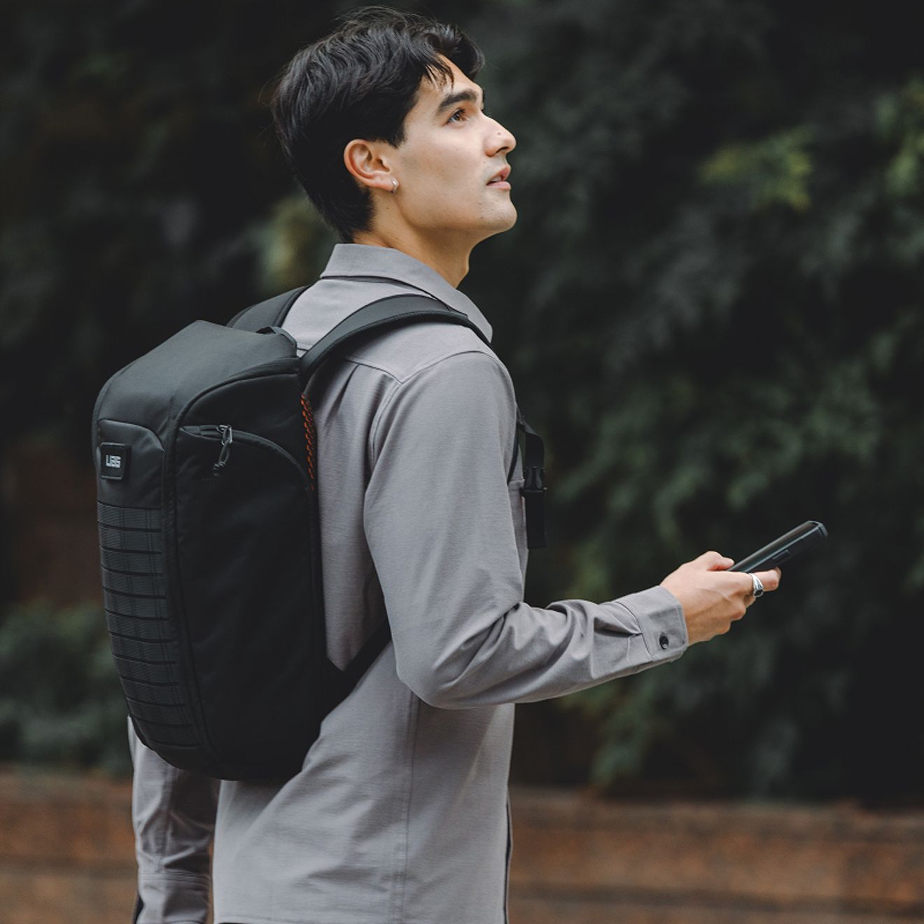 A person wearing a black UAG backpack holds a smartphone while walking outdoors.
