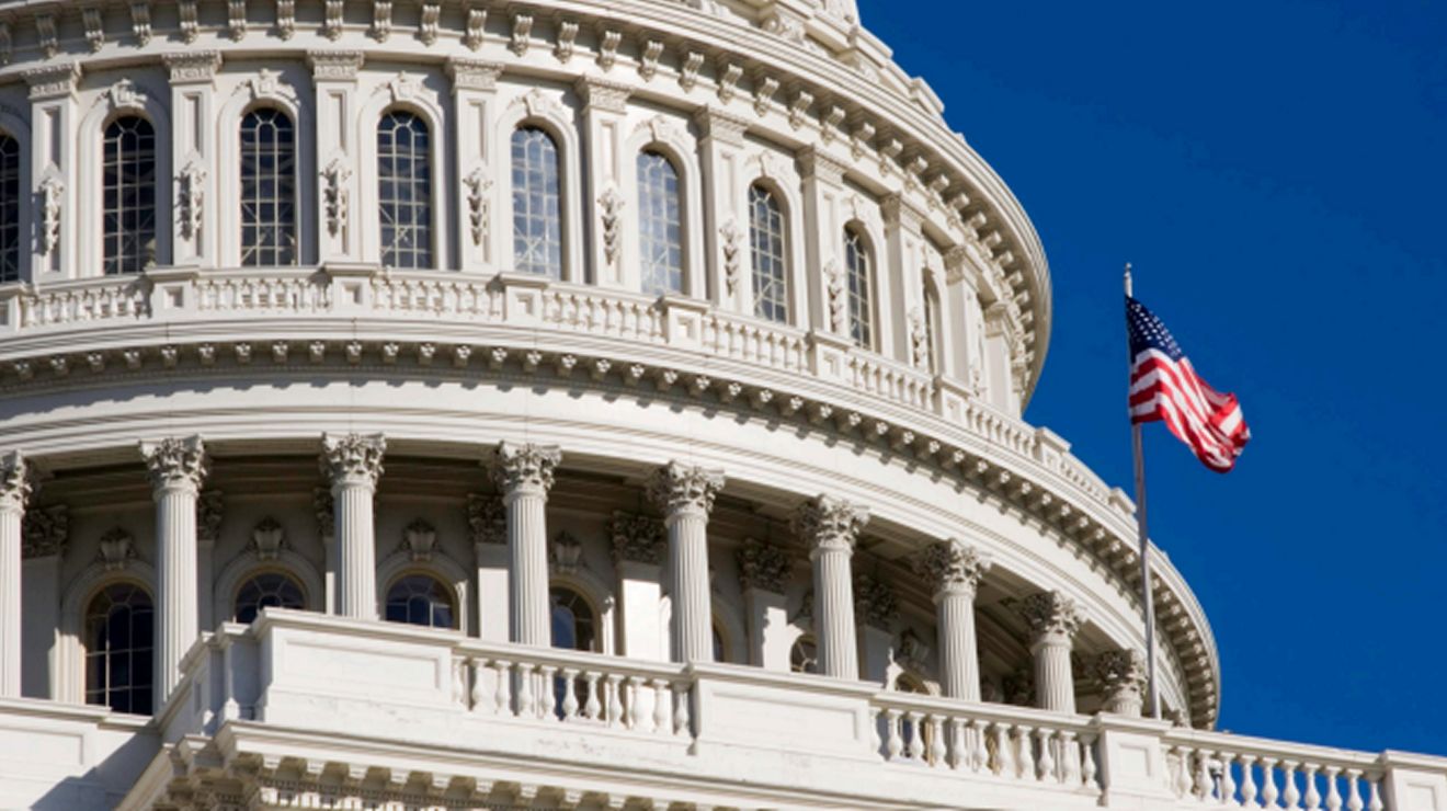 Close up of the U.S. Capitol dome and American flag against a blue sky.