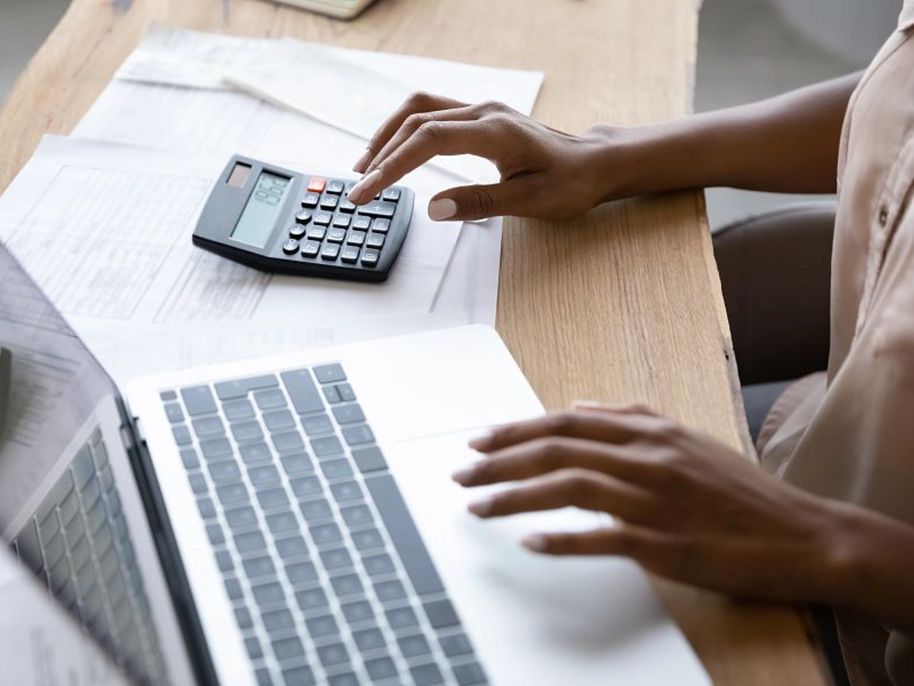 A person using a laptop with their left hand and a calculator with their right hand.