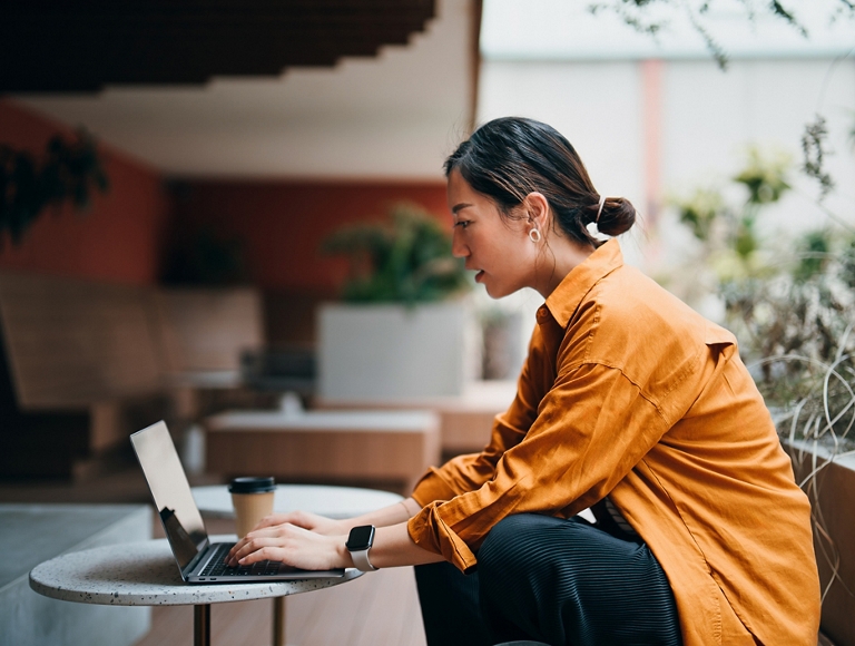 A business professional works on their laptop in a building lobby with a coffee on the table.