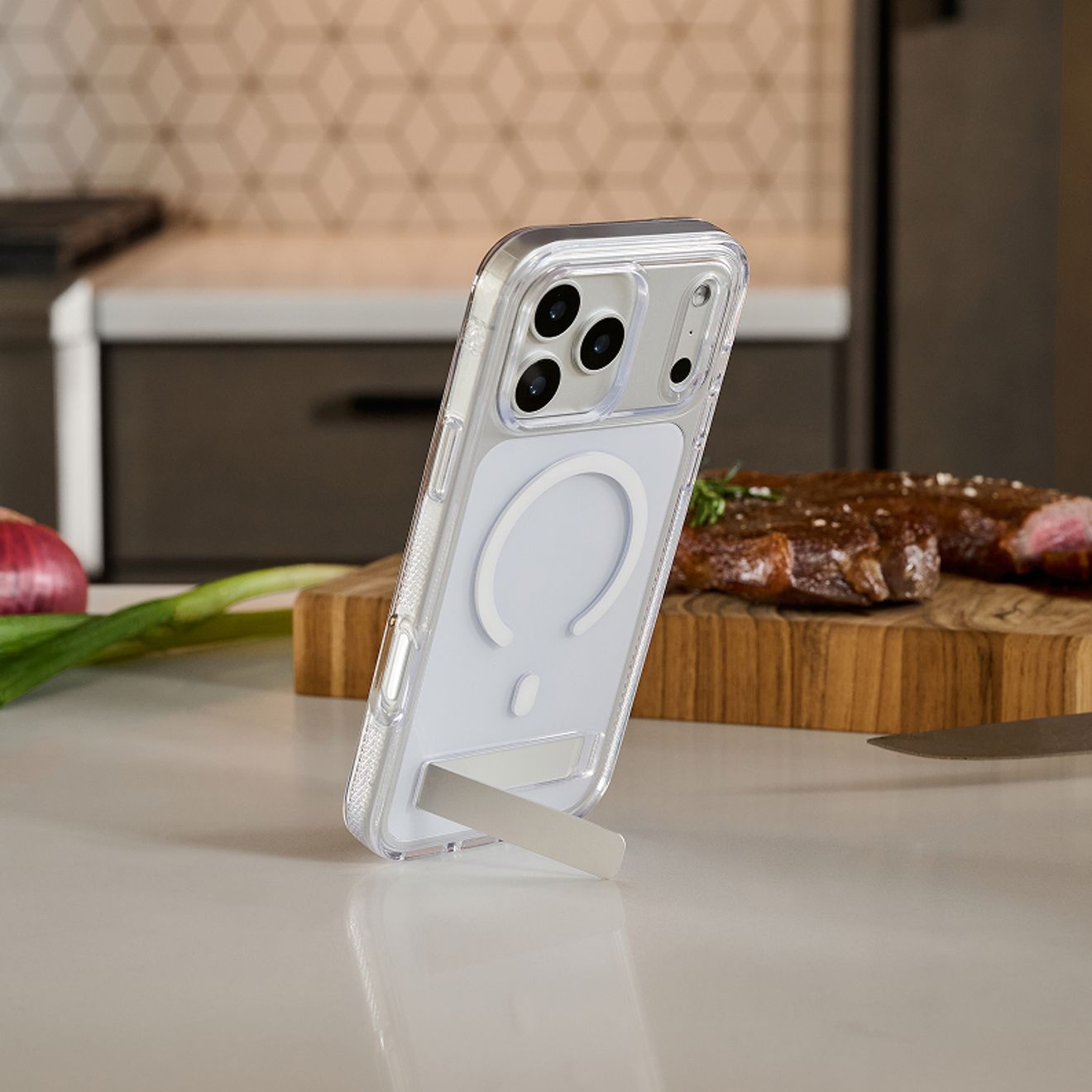 A silver iPhone 17 Pro in a clear ZAGG Crystal Palace case with a white magnetic charging ring and built-in kickstand stands upright on a kitchen counter.