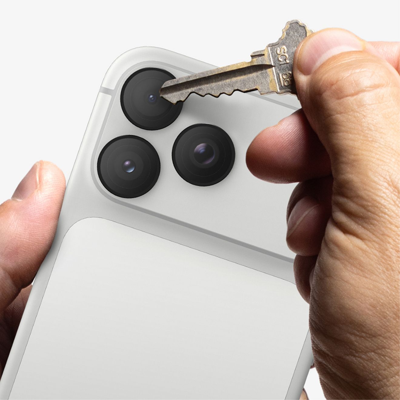 A hand presses a metal key against one of the rear camera lenses of a silver iPhone Pro protected by a ZAGG Glass Elite Camera Lens Protector, demonstrating scratch protection.