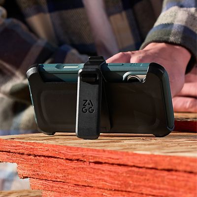 Close-up of a silver iPhone 17 Pro in a blue ZAGG Teton protective case secured in a black ZAGG holster with a belt clip, resting on a wooden surface.