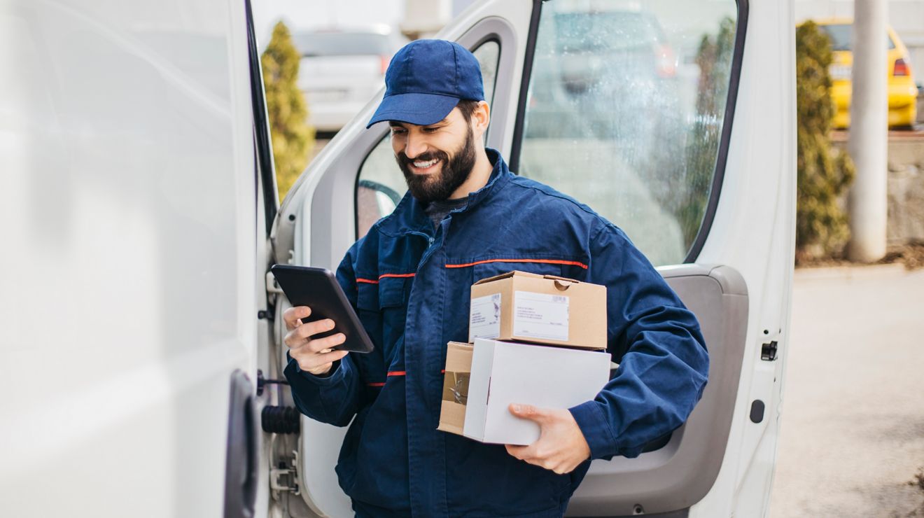 A delivery driver checks their 5G-connected tablet while standing beside their van.