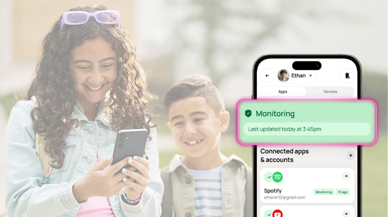 A young girl and a boy are smiling. Both are looking at the smartphone the girl is holding.  