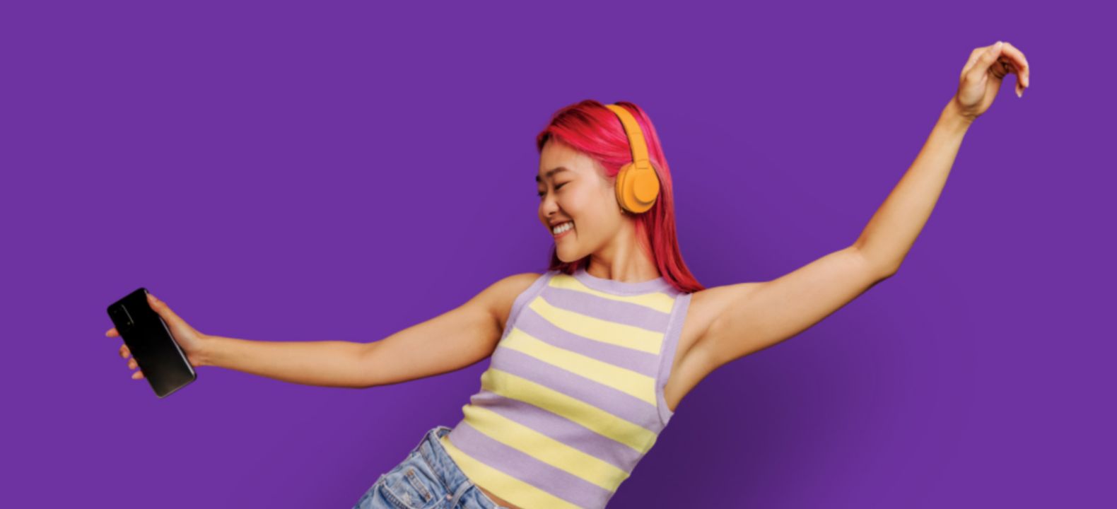 Woman wearing headphones, holding smart phone, and dancing.