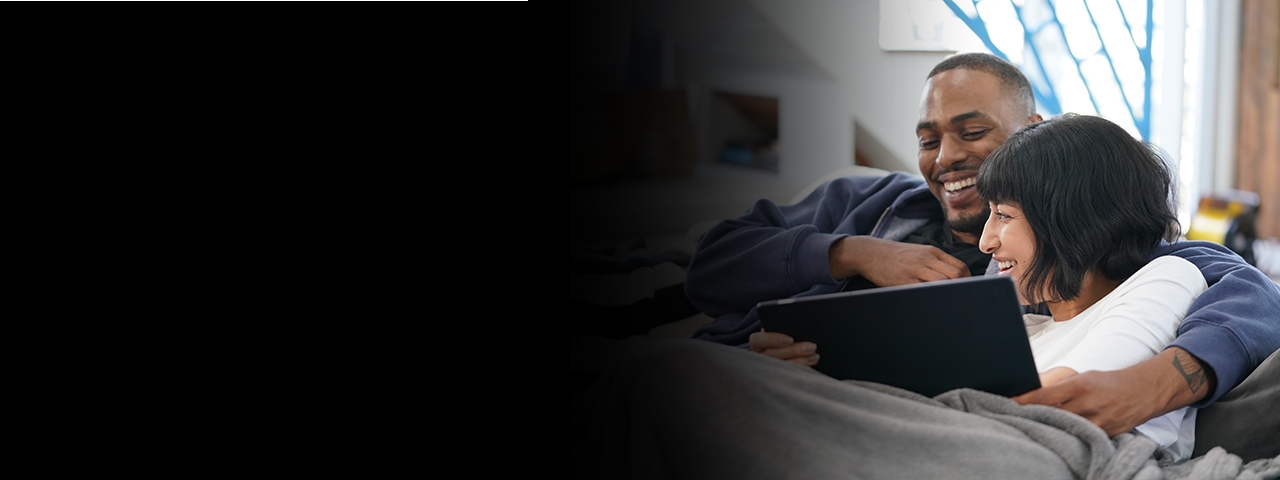 Man and woman laugh while watching tablet