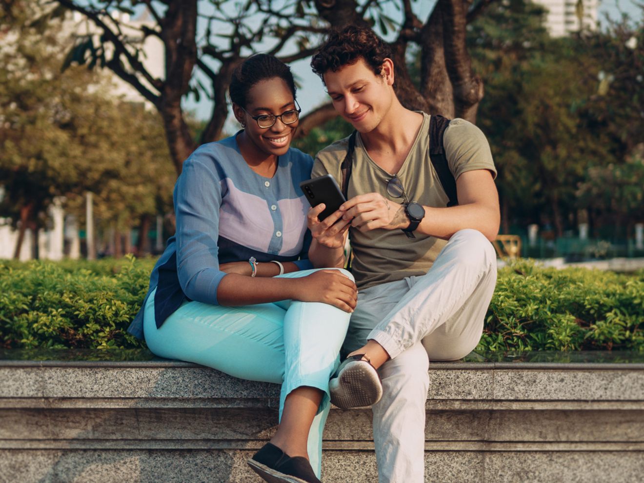 Two people sitting in a park, looking at a smartphone.