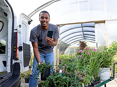 Man smiling and holding a REVVL phone outside of a greenhouse.