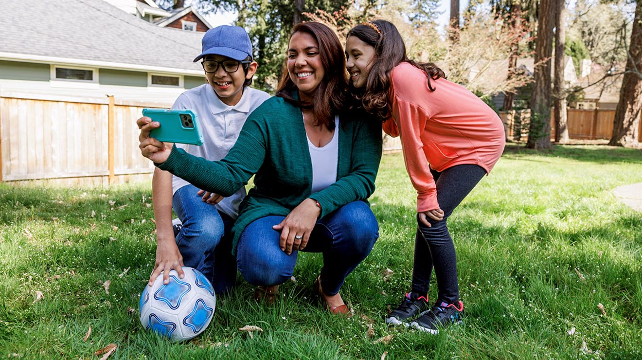 A woman and two children outside, looking at a mobile phone.