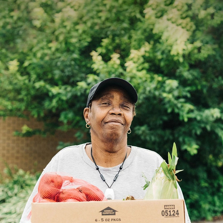 A woman holding a box of vegetables and smiling.