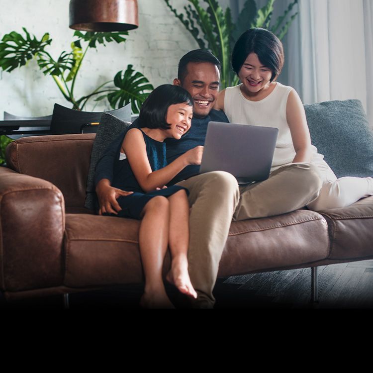 A family sits together on the couch and shares a laptop.
