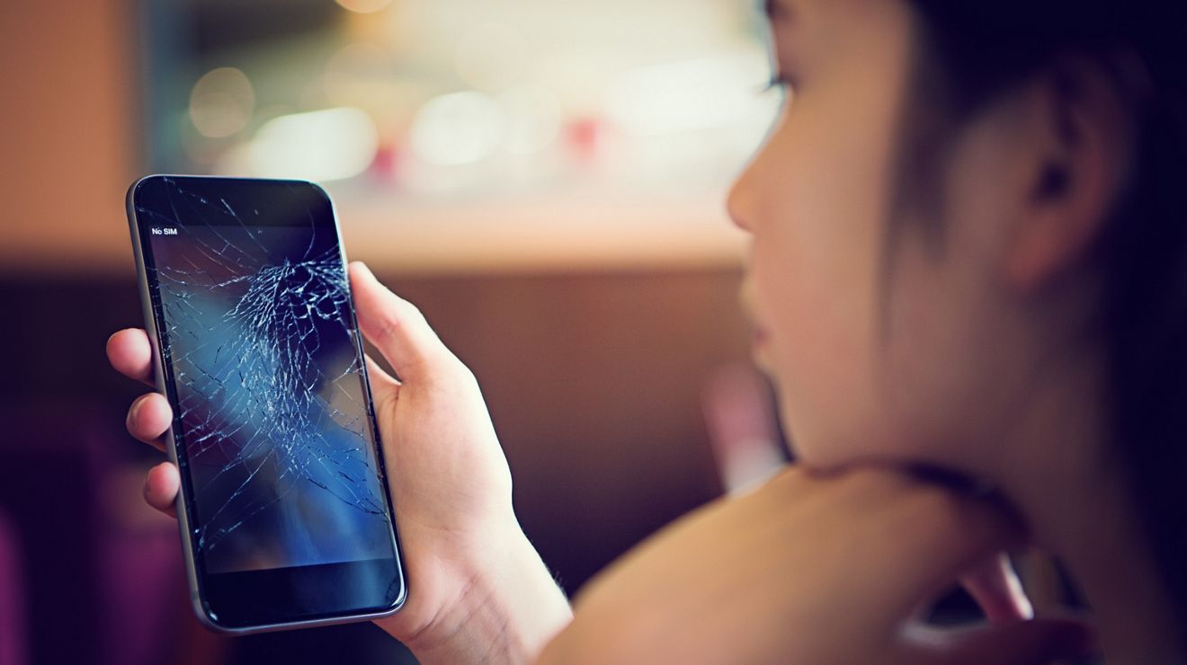 A woman stares at her cracked smartphone screen.