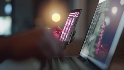 Person looking at computer code on phone and laptop.